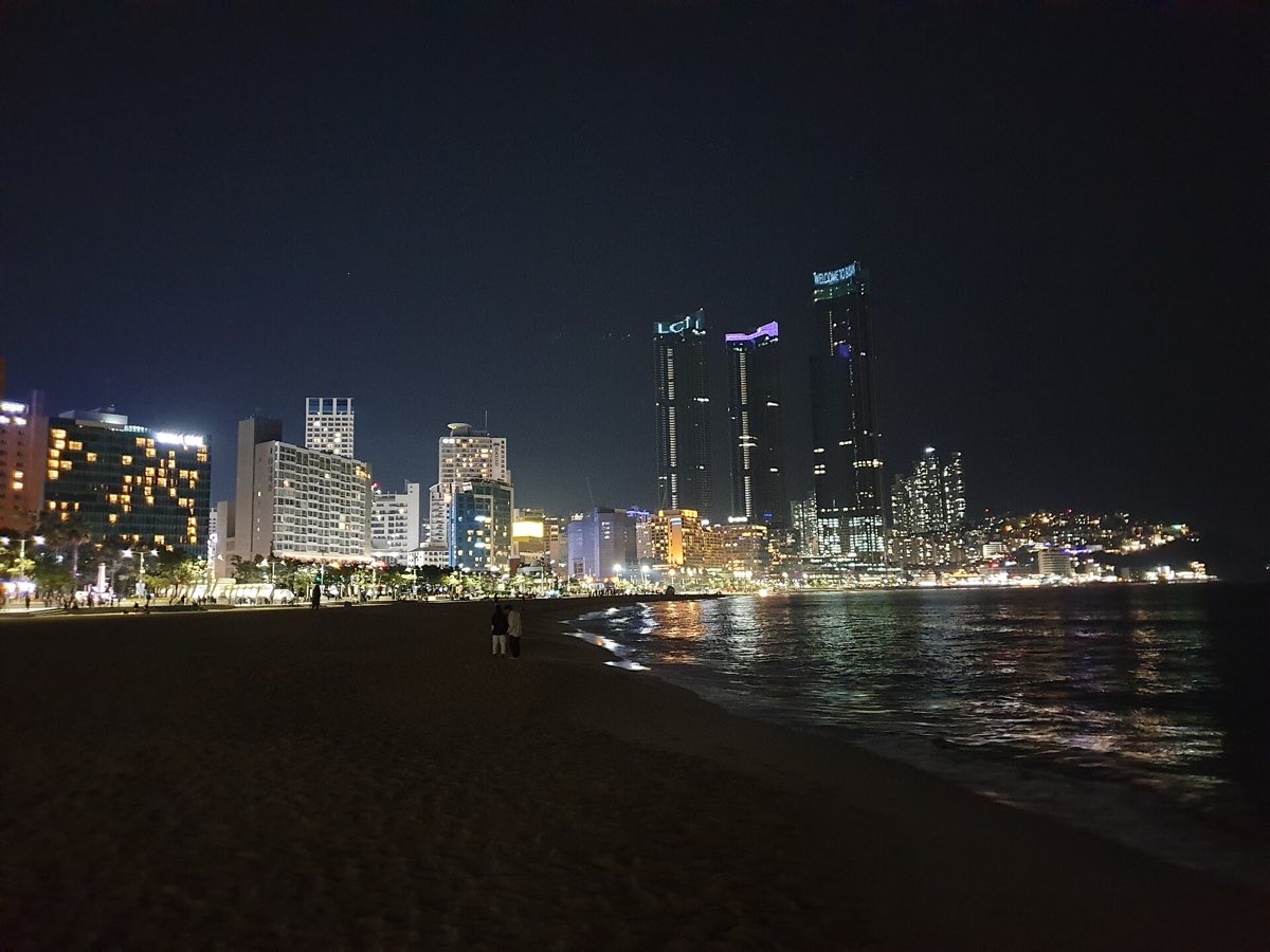 Haeundae Beach at night with the lit city skyline behind the sand