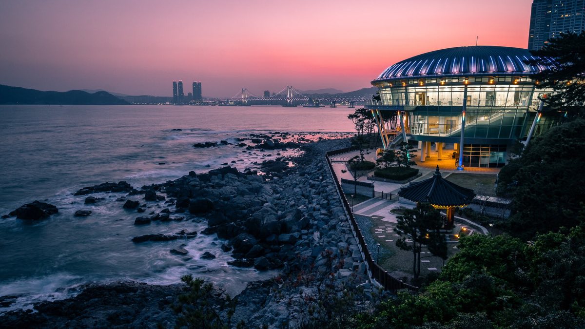 Busan at blue hour — the rocky Dongbaekseom shore with the city lights coming on